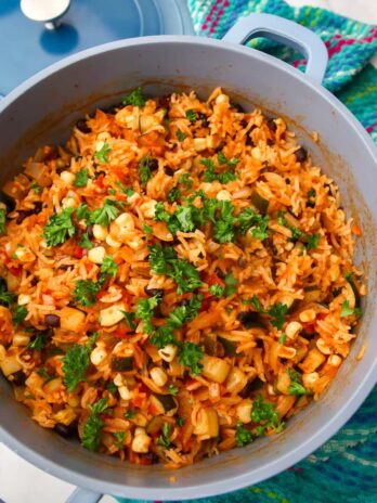 A blue pot filled with vegan Mexican rice with corn, beans, zucchini and salsa in it.
