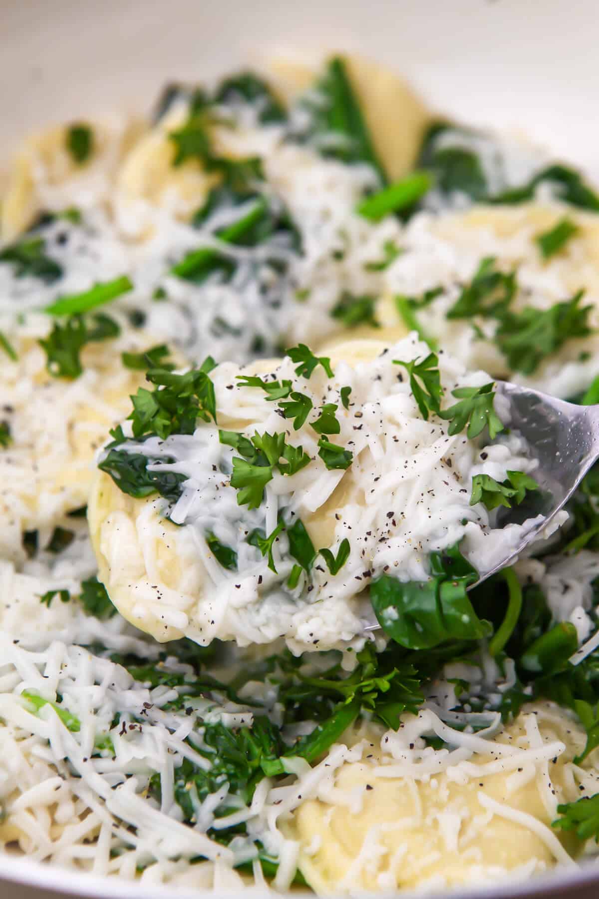 A frying pan full of dairy free perogies topped with vegan cheese and sprinkled with parsley being scooped up in a spoon.