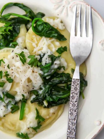 A white plate filled with vegan pierogies with spinach and cheese.