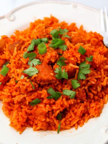 A top view of a white plate filled with vegan red rice with cilantro and green onions sprinkled on top.