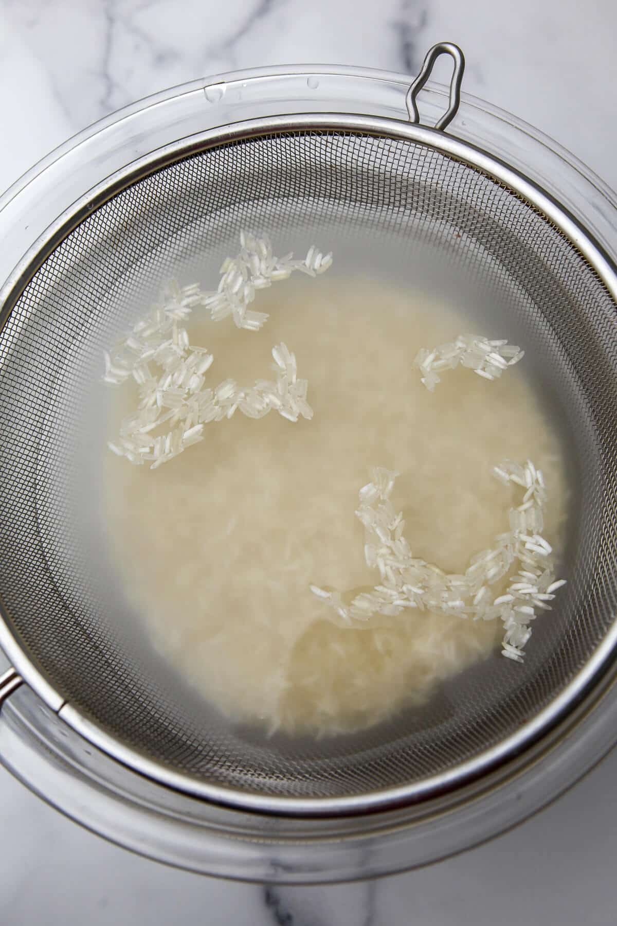 Basmati rice being washed in a mesh strainer.