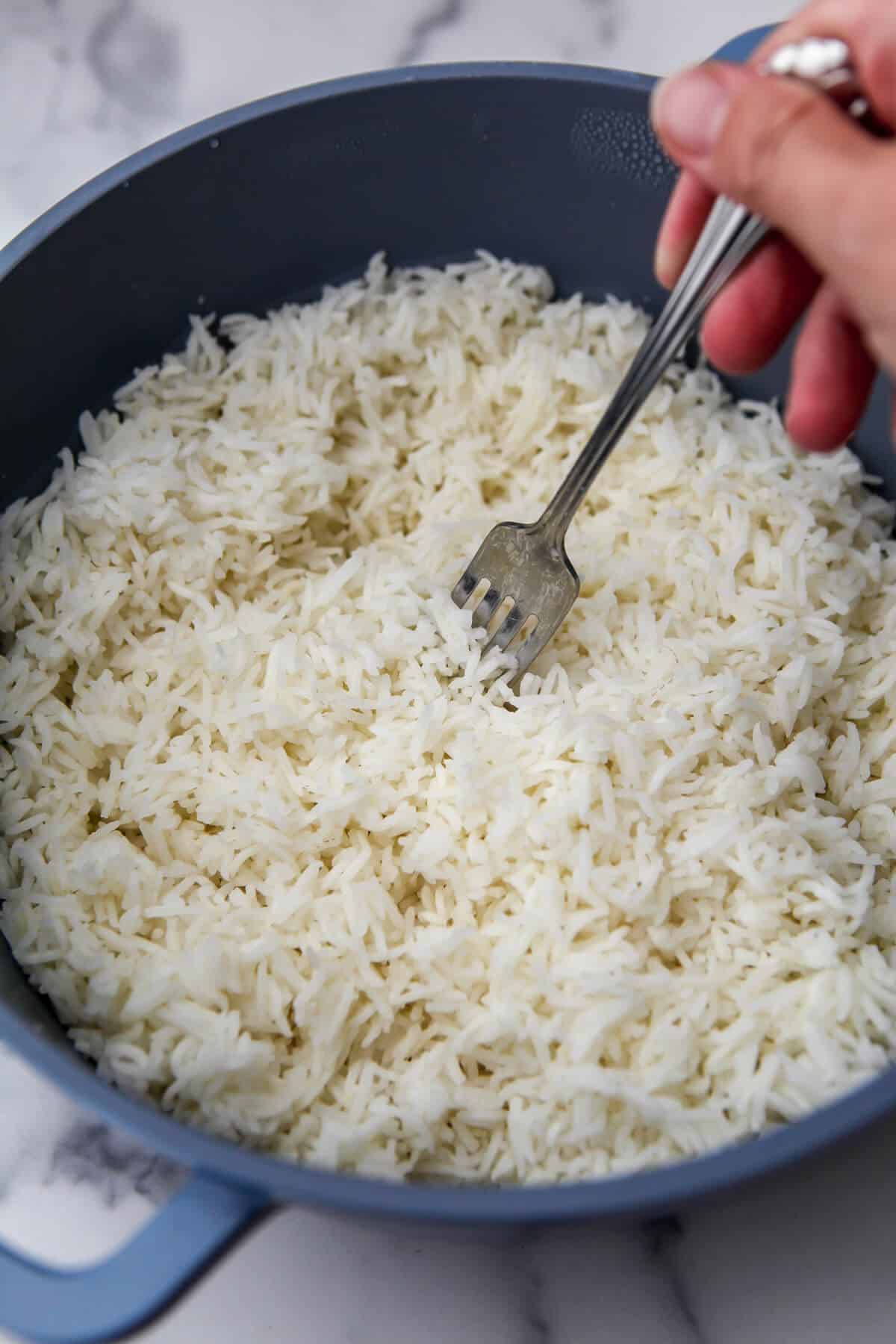 Fluffing Basmati rice with a fork after cooking.