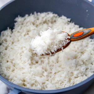 A blue pot filled with cooked basmati rice with some being scooped up in a colorful wooden spoon.