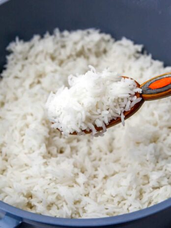 A blue pot filled with cooked basmati rice with some being scooped up in a colorful wooden spoon.