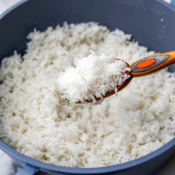 A blue pot filled with cooked basmati rice with some being scooped up in a colorful wooden spoon.