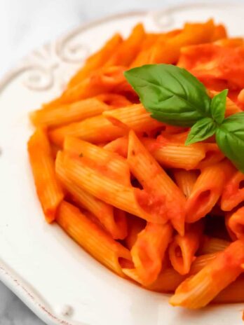 Vegan roasted tomato and pepper sauce over pene pasta with a basil leaf on top.