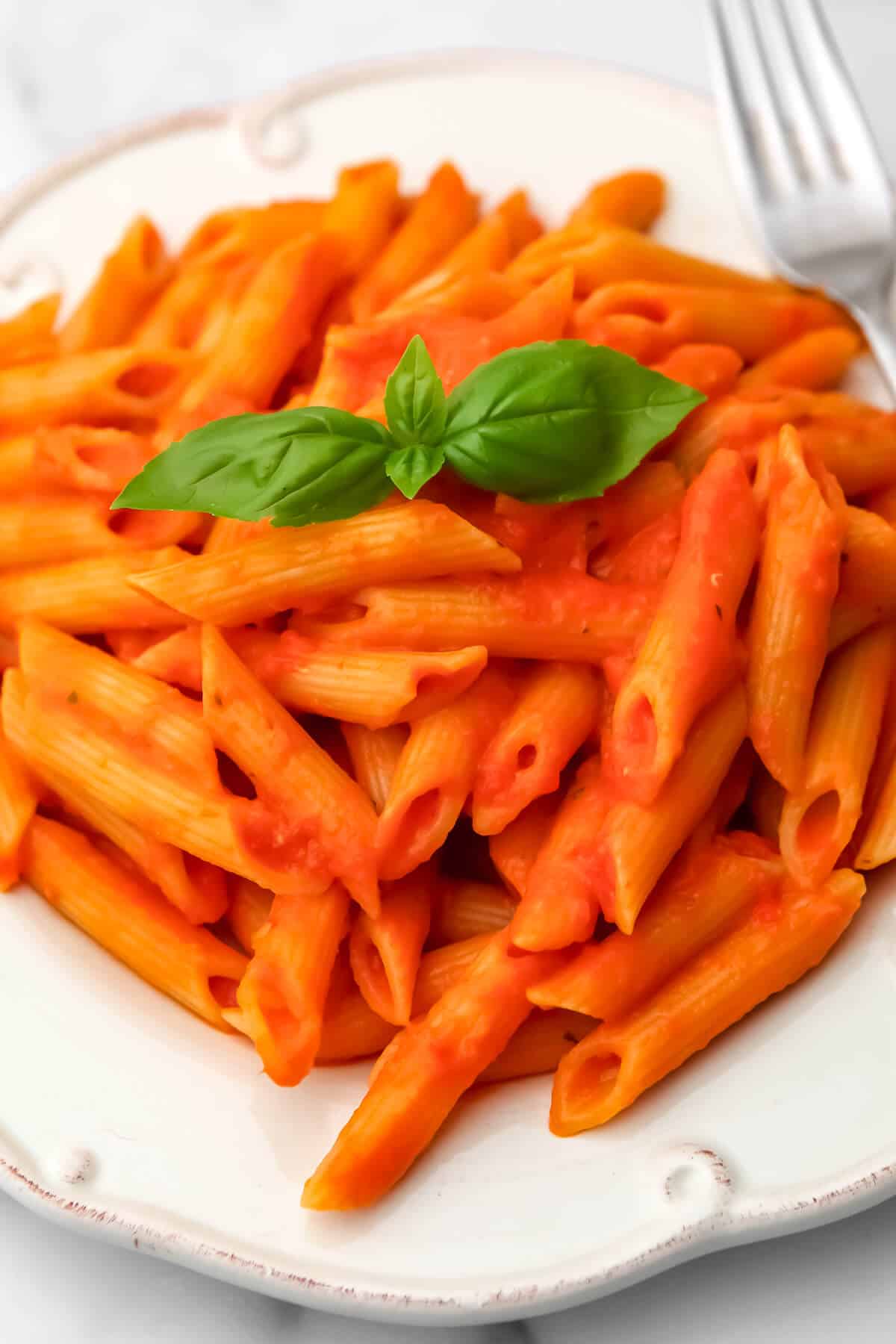 Roasted red pepper and tomato sauce mixed with pene pasta served on a white plate with a fork on the side.