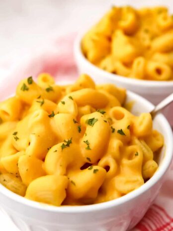 Two bowls of vegan pumpkin mac and cheese with a red and white tea towel on the side.
