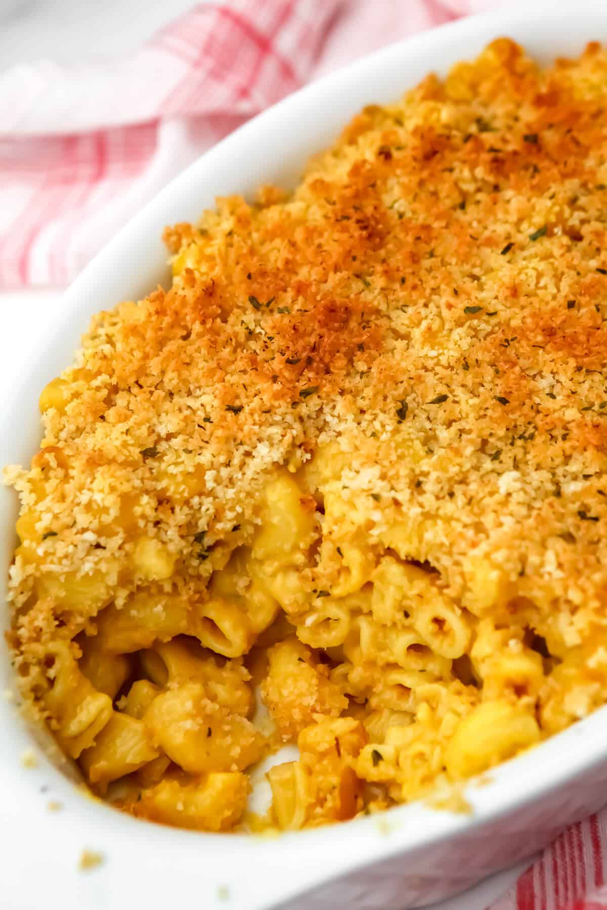 A white casserole dish filled with baked vegan mac and cheese with breadcrumbs on top.