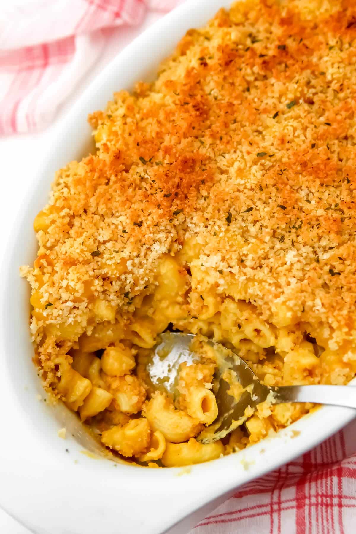A white casserole dish filled with baked vegan mac and cheese with a large spoon in it.