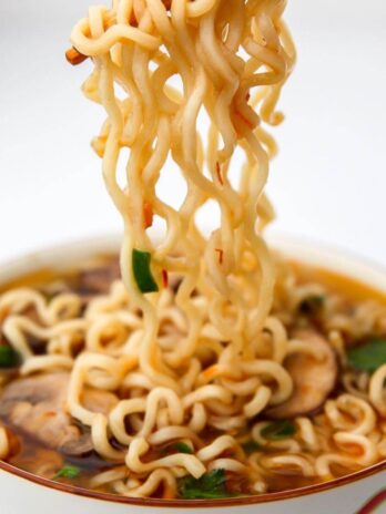 A bowl of ramen noodle soup with the noodle being lifted out with chopsticks.