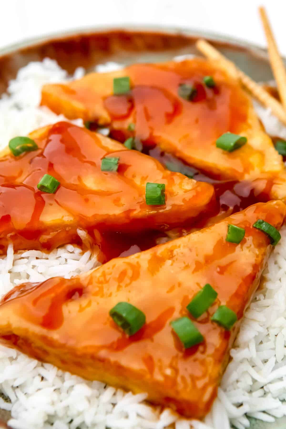 A close up of sweet sticky tofu on a bed of white rice.