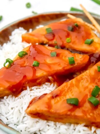 A close up of sticky tofu over rice with green onions sprinkled on top.