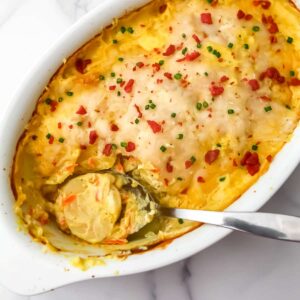 A top view of a vegan potato bake with a spoon resting where some of the casserole has been scooped out.