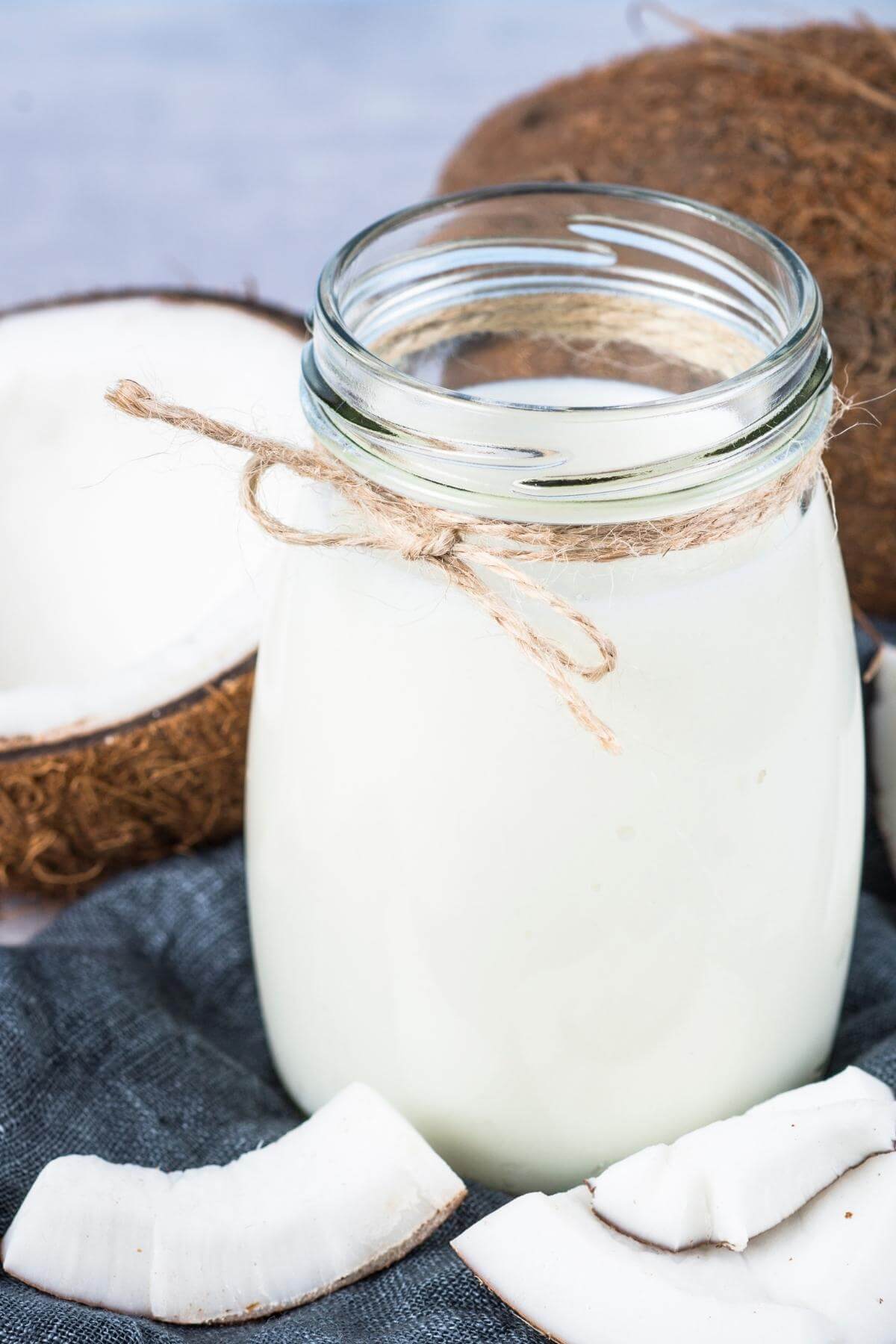 A glass of coconut milk with open coconuts behind it.