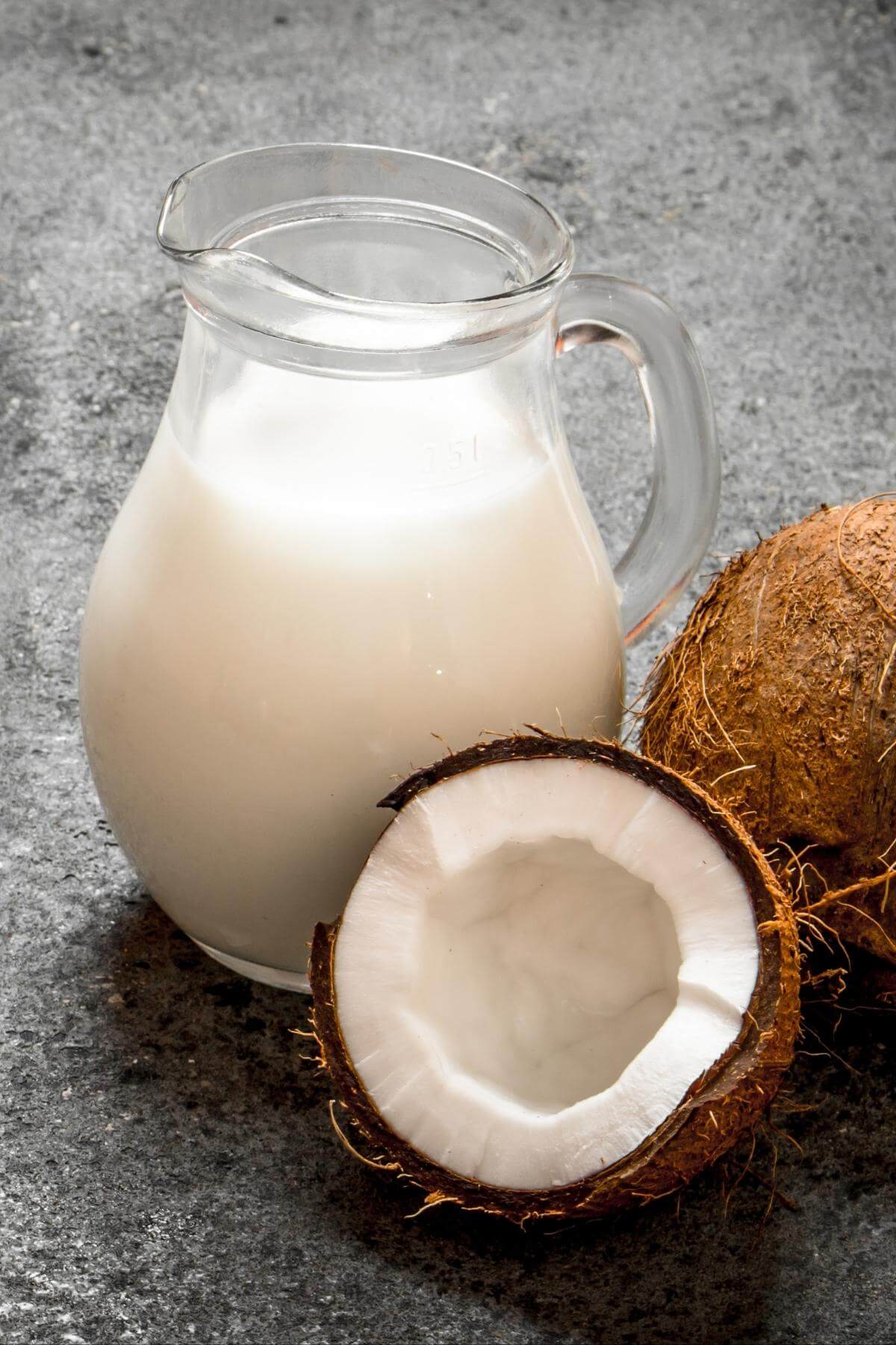 A pitcher of coconut milk next to two coconuts.