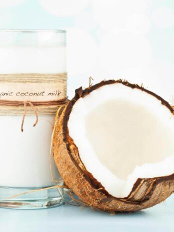 A glass of coconut milk next to an open coconut.