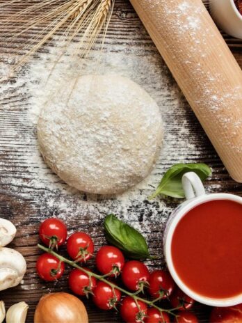 Vegan pizza dough with tomato sauce, tomatoes, and mushrooms on the side.
