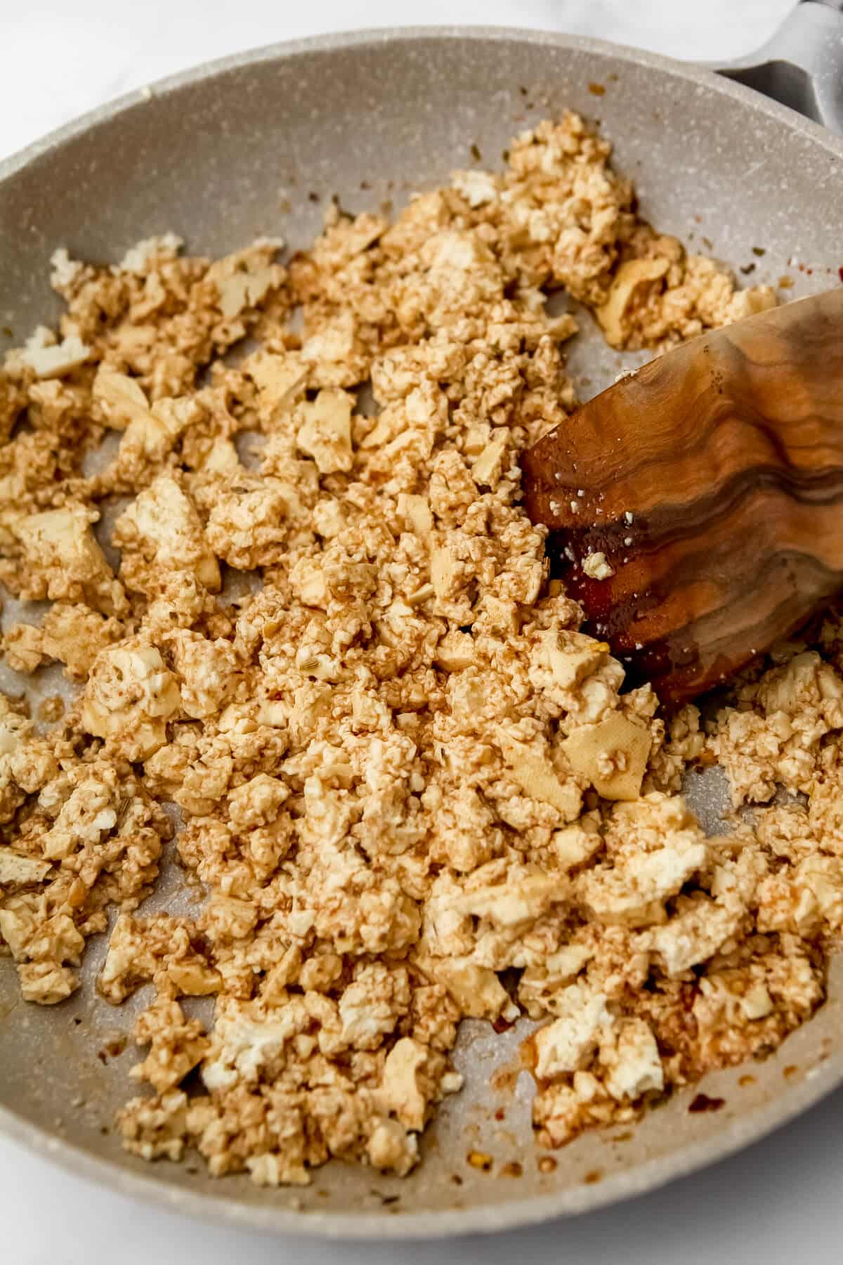 Tofu sausage frying in a pan and being stirred with a wooden spatula.