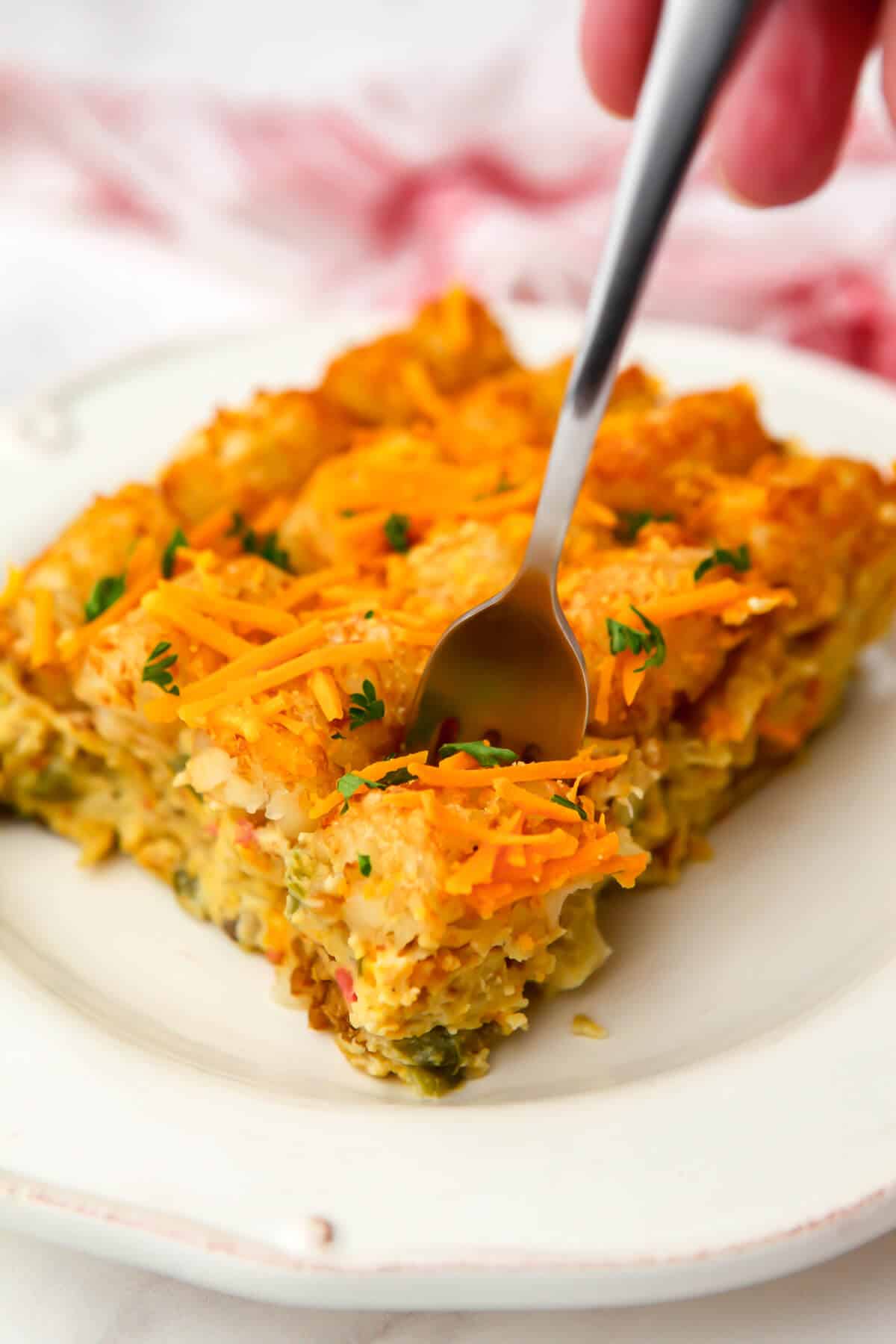 A serving of vegan breakfast casserole on a white plate with a fork in it.