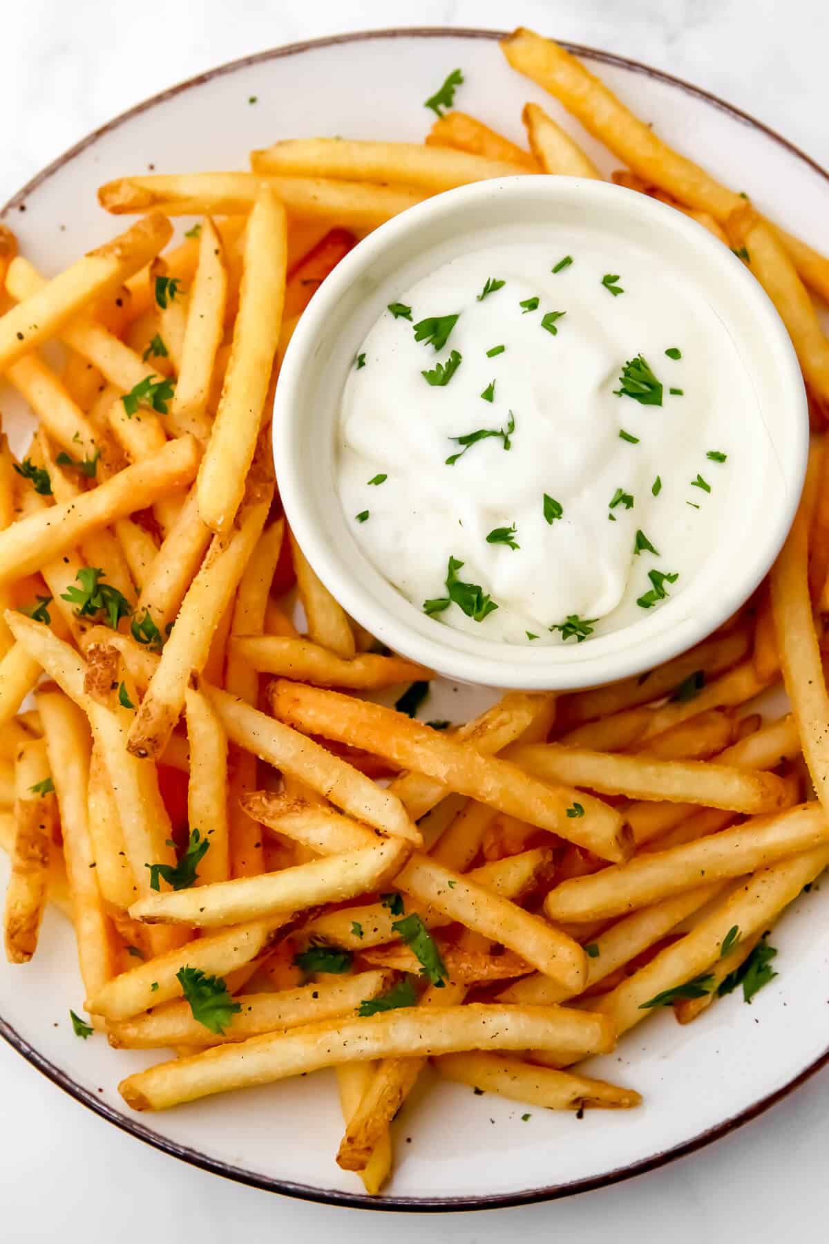 A top veiw of a bowl of dairy-free garlic aioli with French Fries.