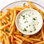 A small bowl of vegan garlic aioli with French fries around it.