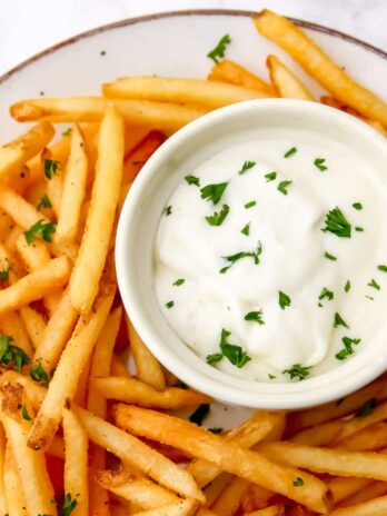 A small bowl of vegan garlic aioli with French fries around it.
