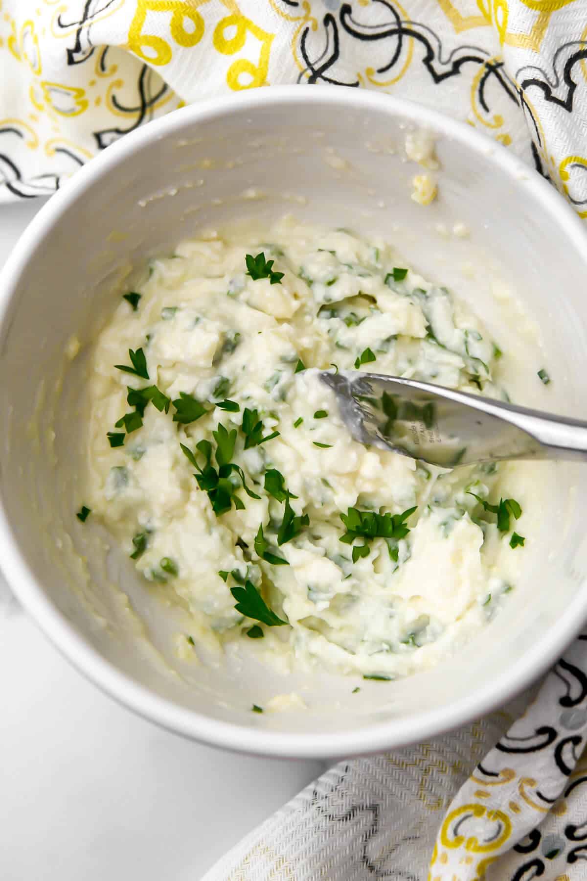 Vegan garlic herb butter in a white bowl with a knife in it.