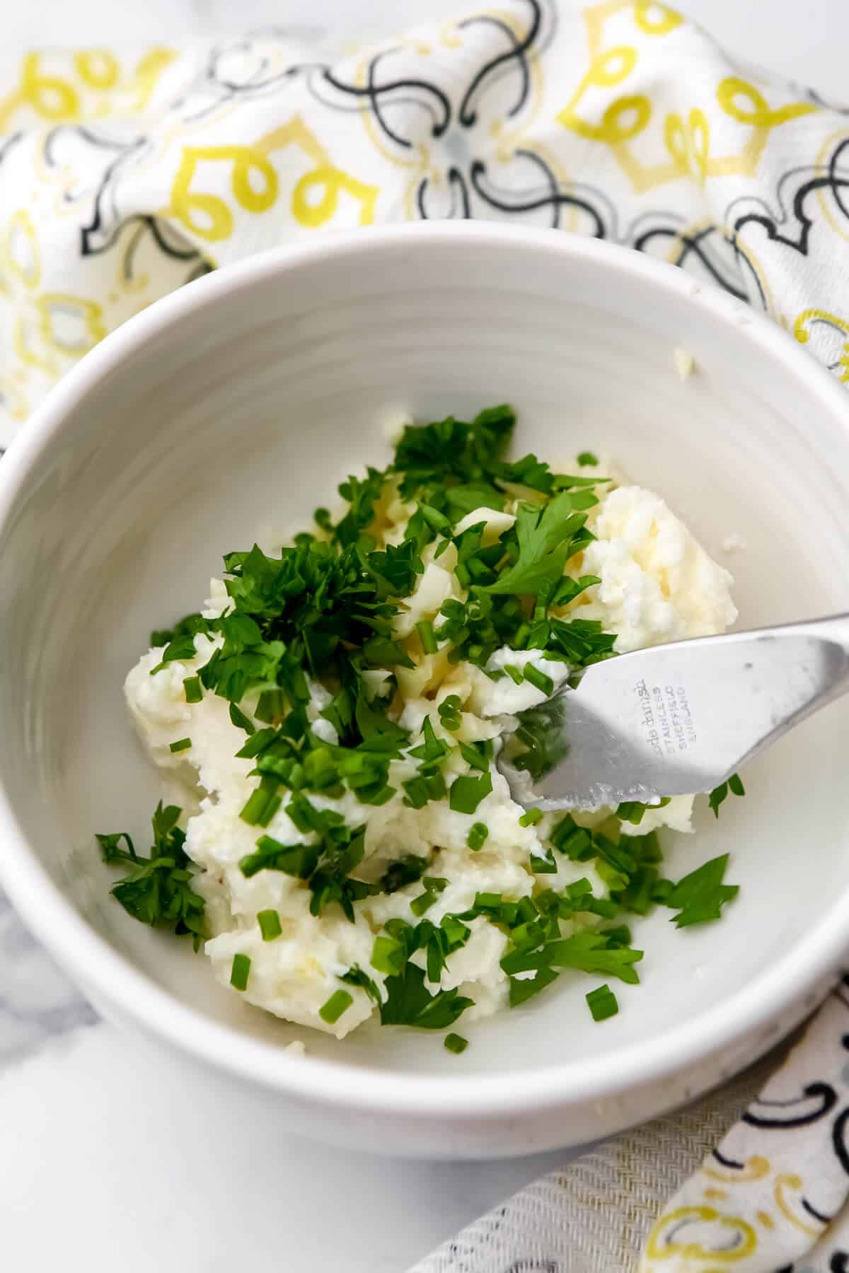 Vegan butter with mined garlic and fresh herbs in a white bowl.