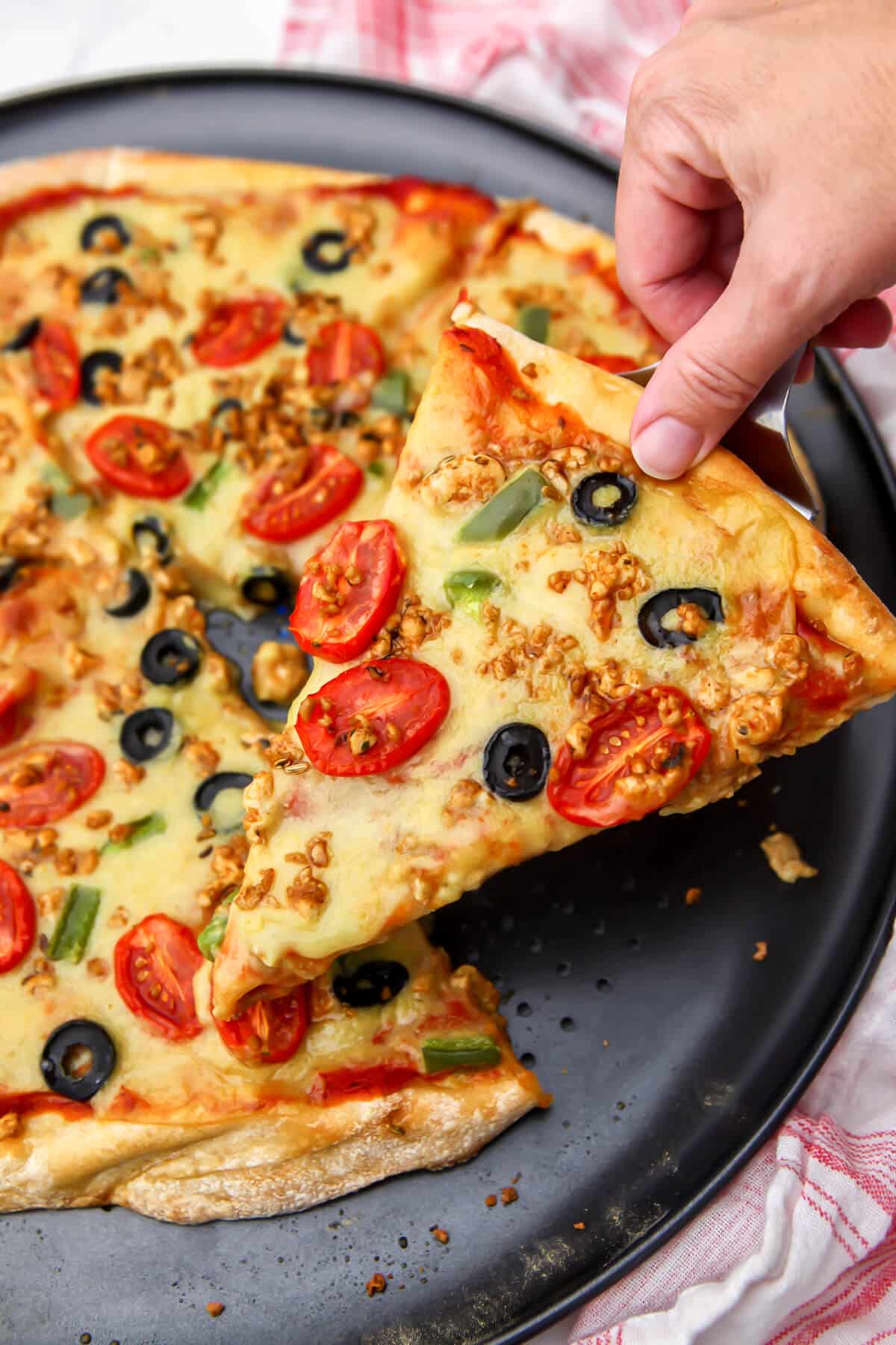 Homemade vegan pizza cheese ona a pizza with tomatoes, black olive, and green peppers.