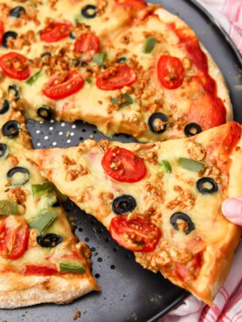 Someone picking up a slice of pizza with homemade vegan pizza cheese on top.