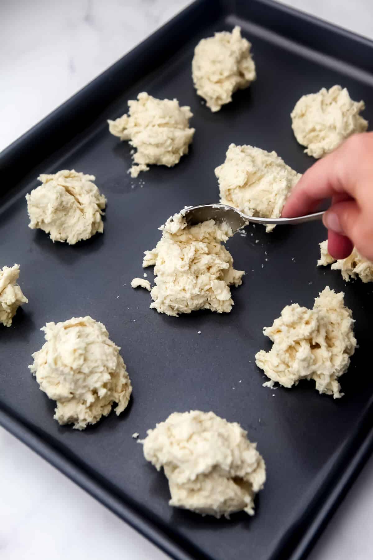 Vegan drop biscuits being dropped onto a baking sheet with a spoon.