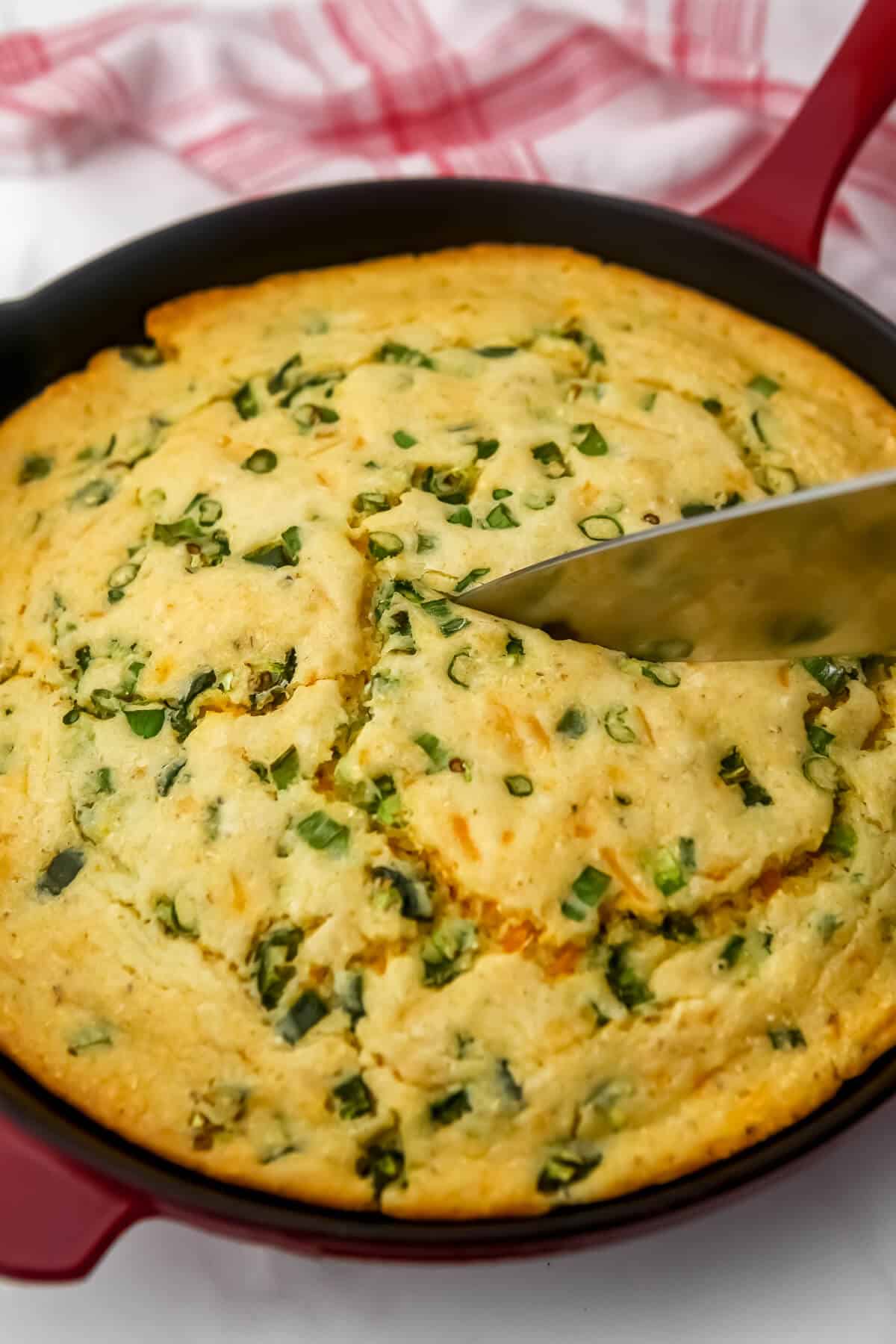 Someone cutting dairy free jalapeno cornbread  with a knife after it has cooled.