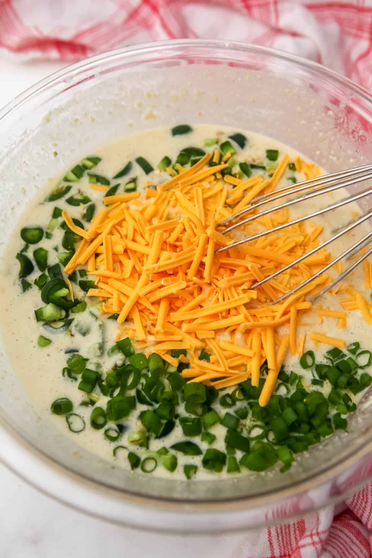 A mixing bowl with vegan cornbread batter, jalapenos, green onions, and vegan cheese.