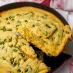 Vegan jalapeno cornbread baked in an iron skillet with a piece being taken out.