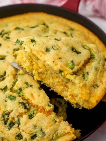 Vegan jalapeno cornbread baked in an iron skillet with a piece being taken out.