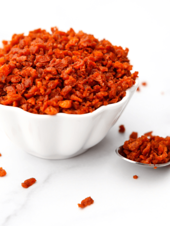 A bowl of vegan bacon bits with a spoon on the side.