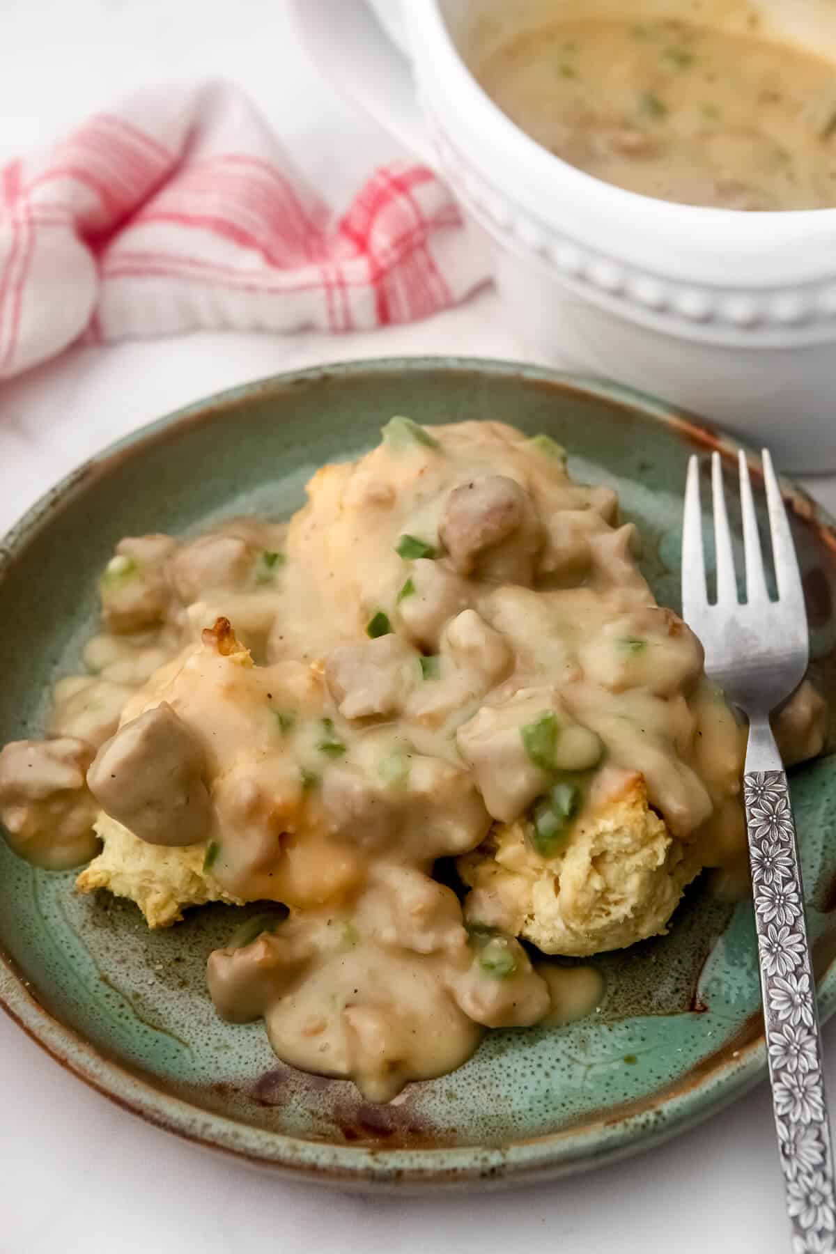 Vegan biscuits with sausage gravy poured over them on a plate with a gravy boat on the side.