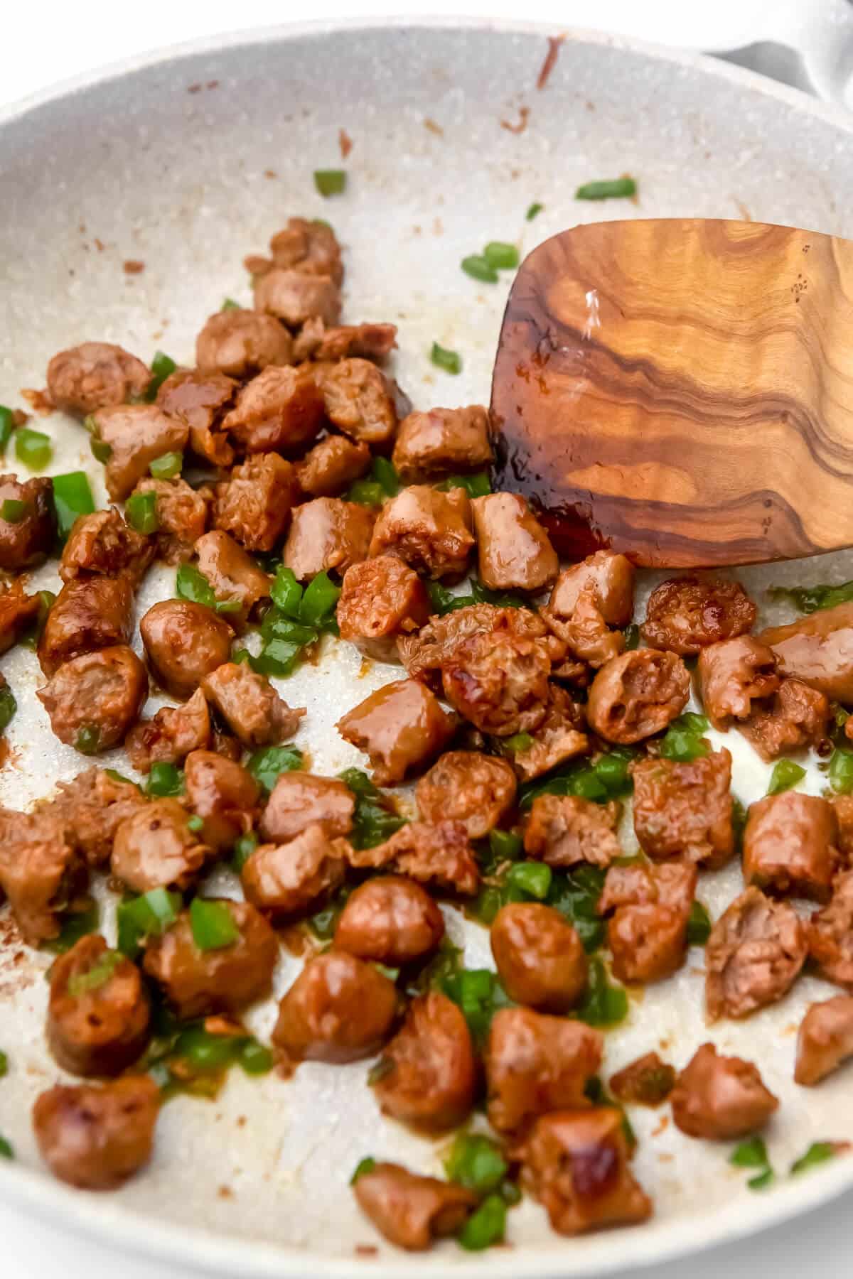 Vegan sausage and green bell pepper being cooked in a skillet.