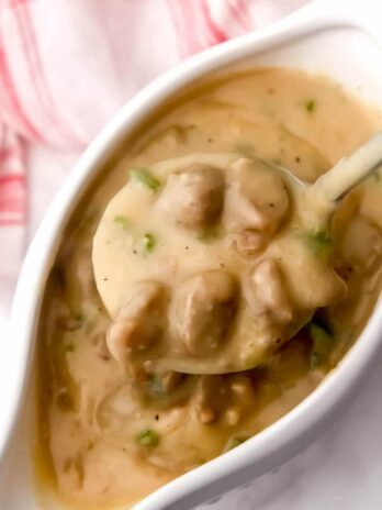 Vegan sausage gravy in a gravy boat being scooped up with a ladel.