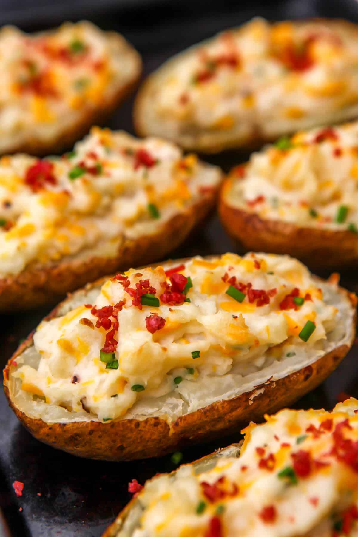 Vegan twice baked potatoes on a baking tray topped with bacon bits, cheese, and chives.