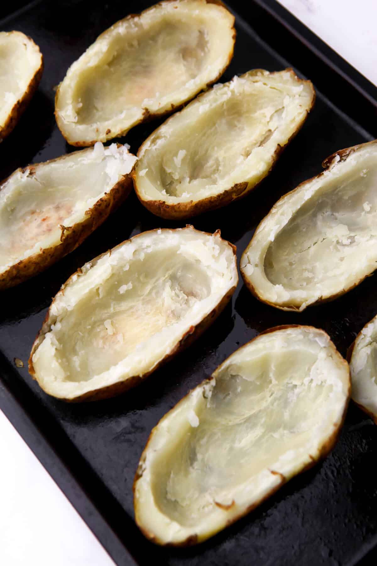 Baked potatoes with the centers scooped out on a baking sheet.