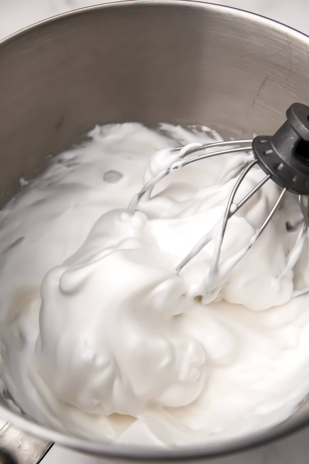 Aquafaba that has been whipped into a meringue in a metal bowl with a whisk attachment.