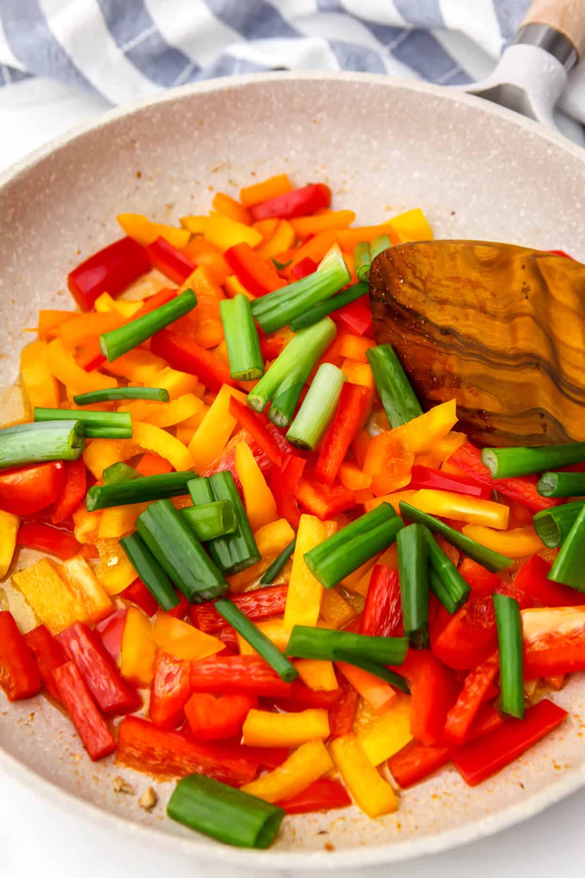 Red bell peppers, yellow bell peppers, and green onions sautéing in a pan.