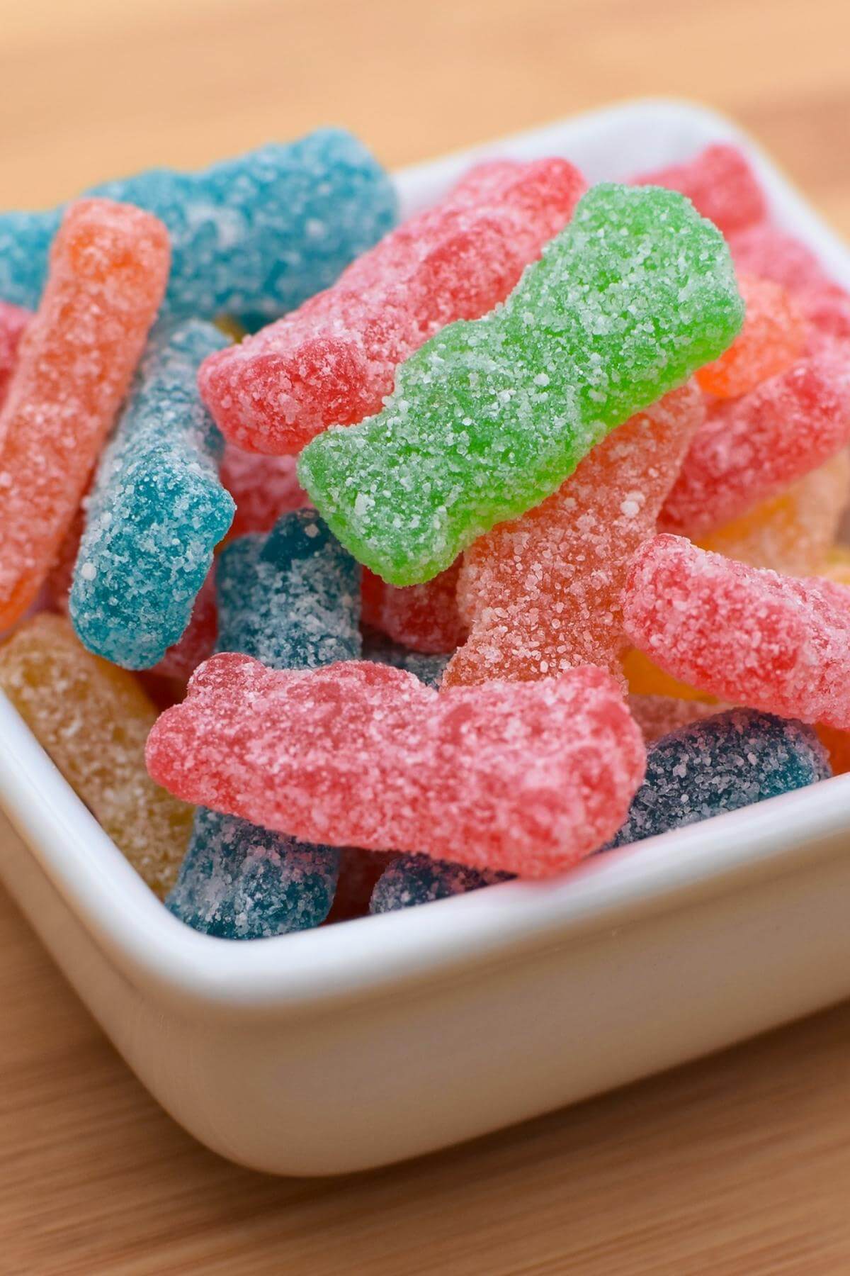 A white square bowl filled with colorful sour patch kids candy.