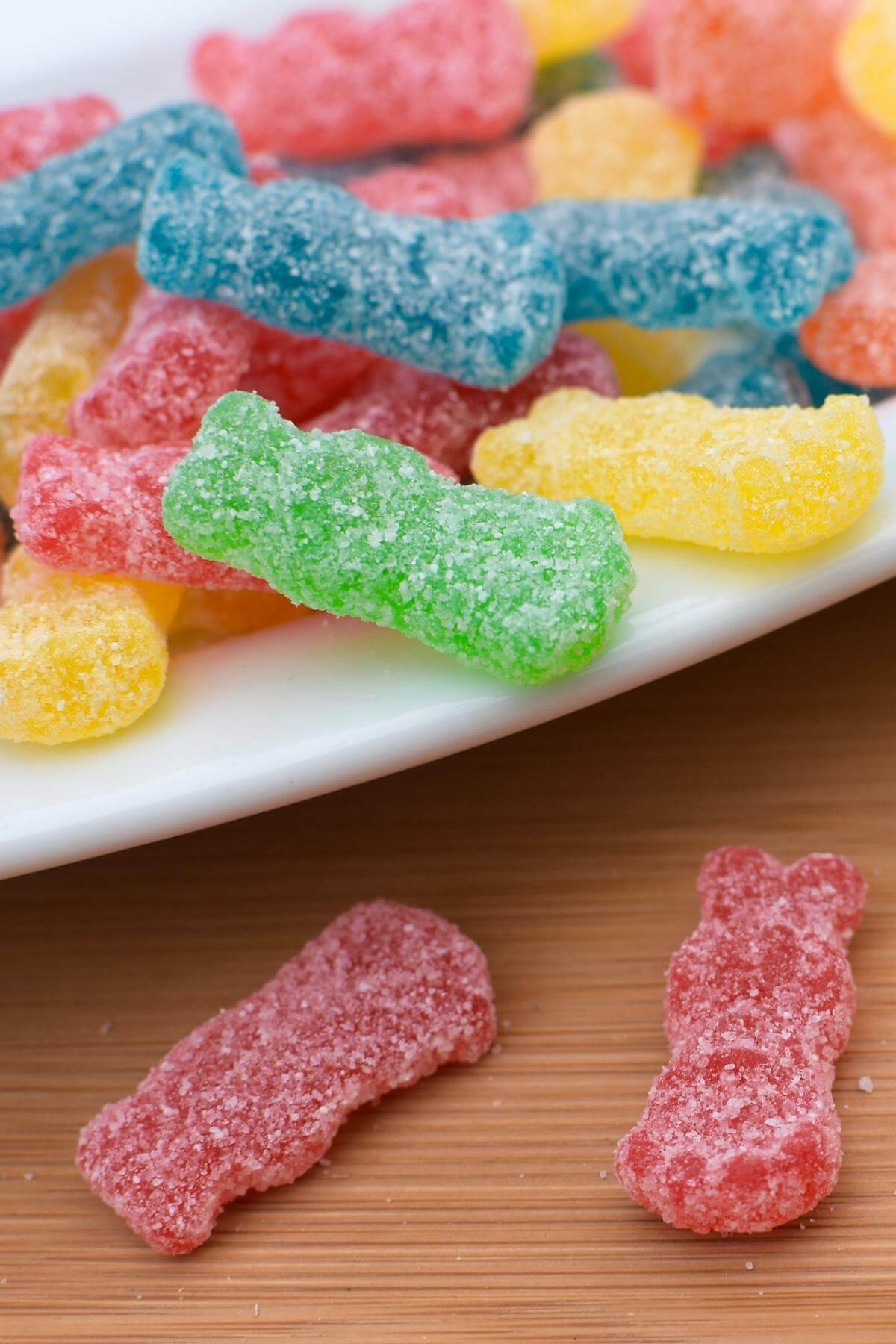 Sour patch kids spilling off of a white plate onto a wooden table.