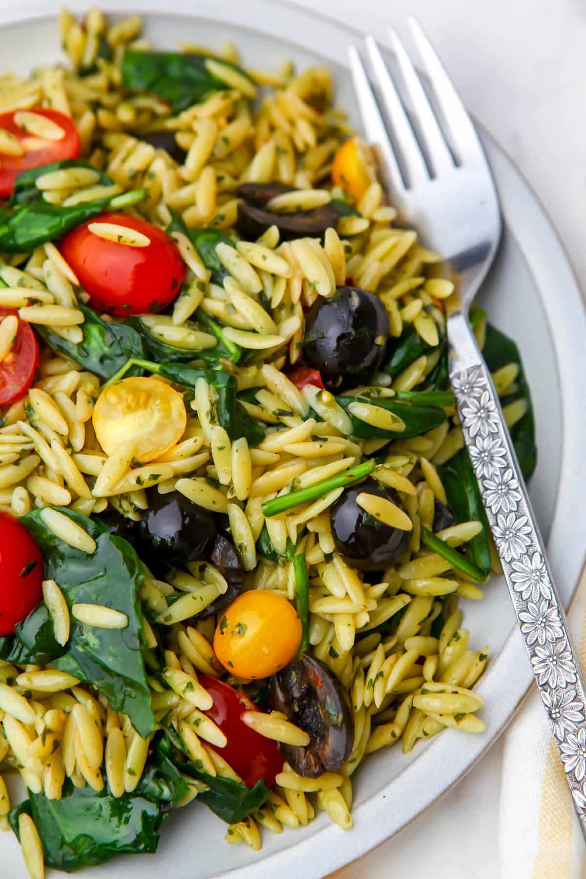 A white plate filled with pesto orzo salad with a fork on the side.