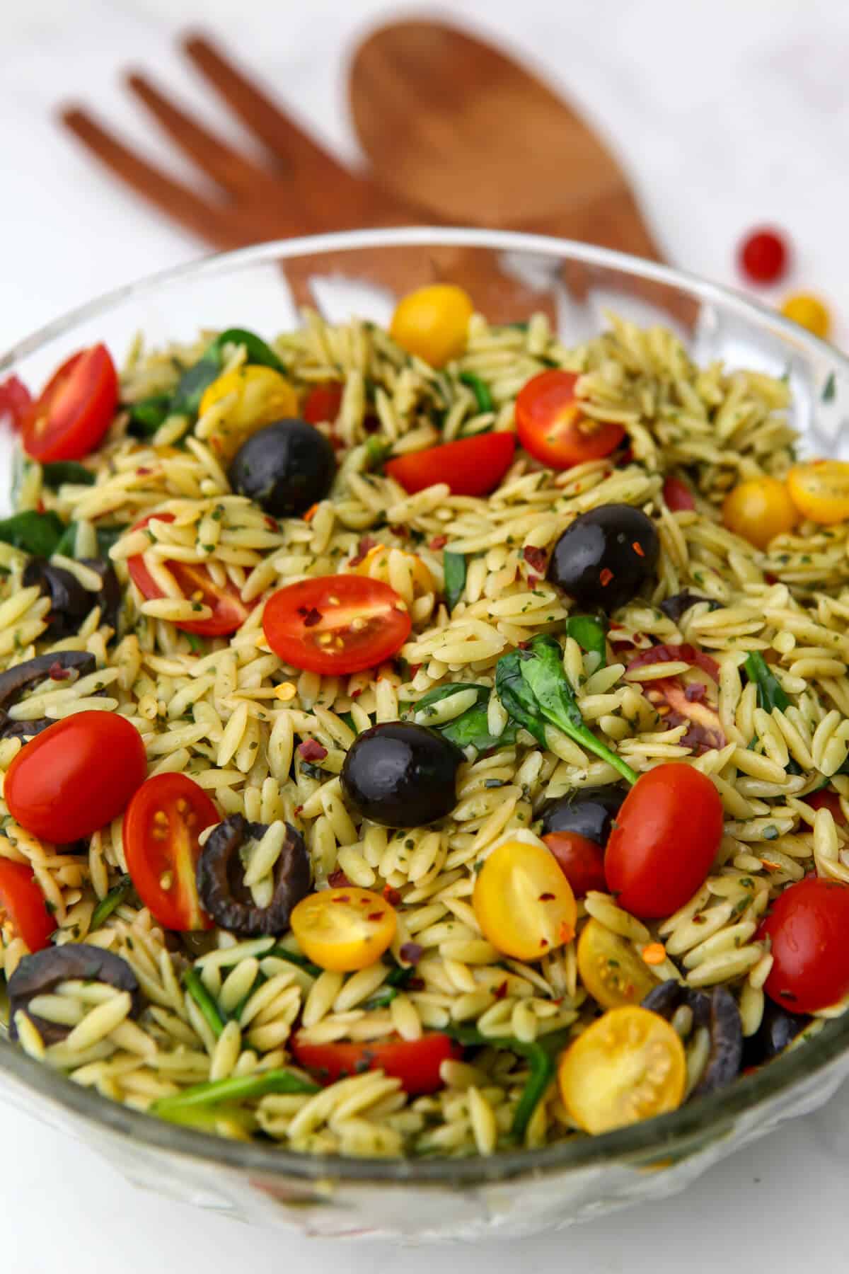 A vegan pesto orzo salad made with spinach, tomatoes, and olives served in a glass salad bowl.