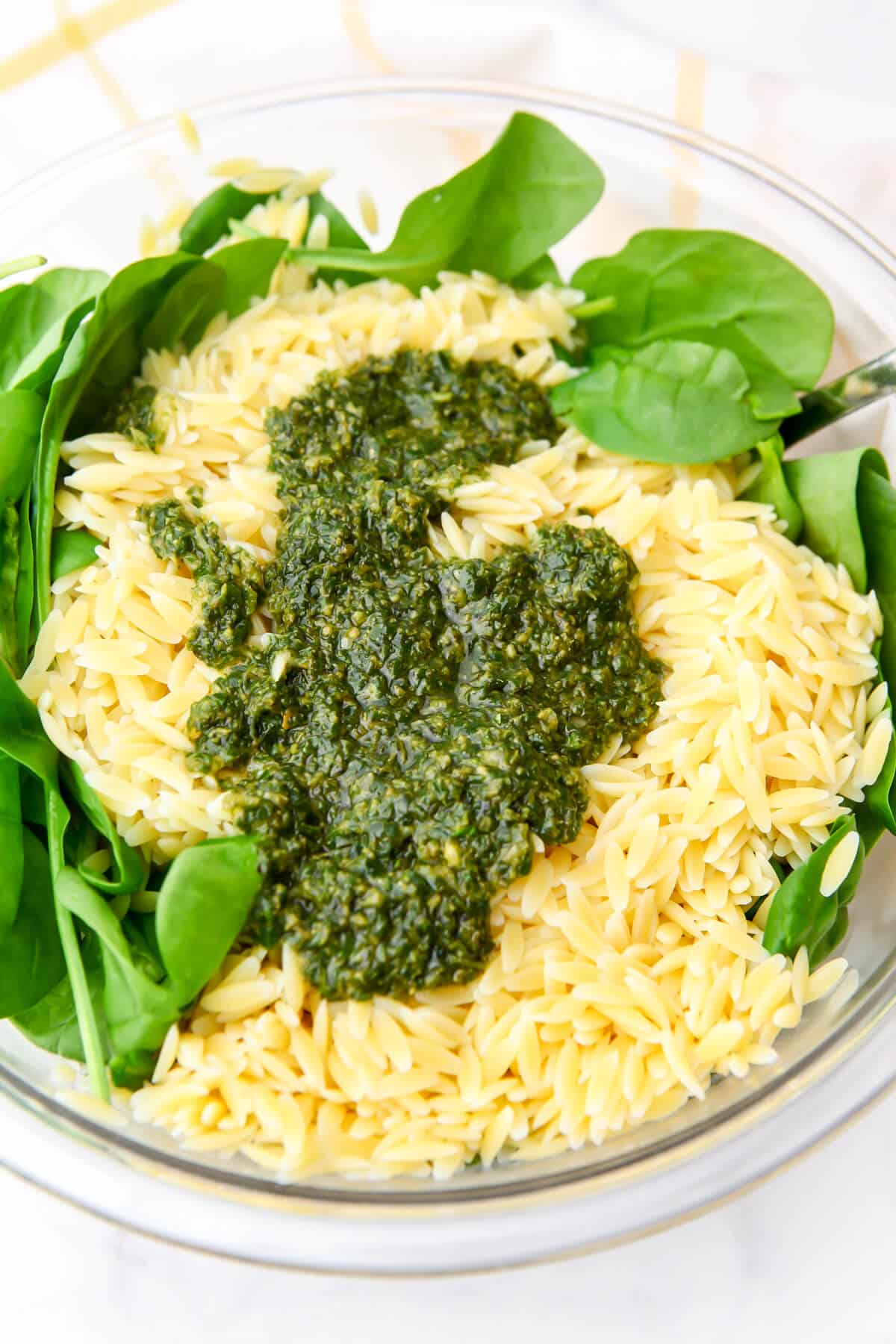 Baby spinach topped with cooked orzo with pesto in a salad bowl.