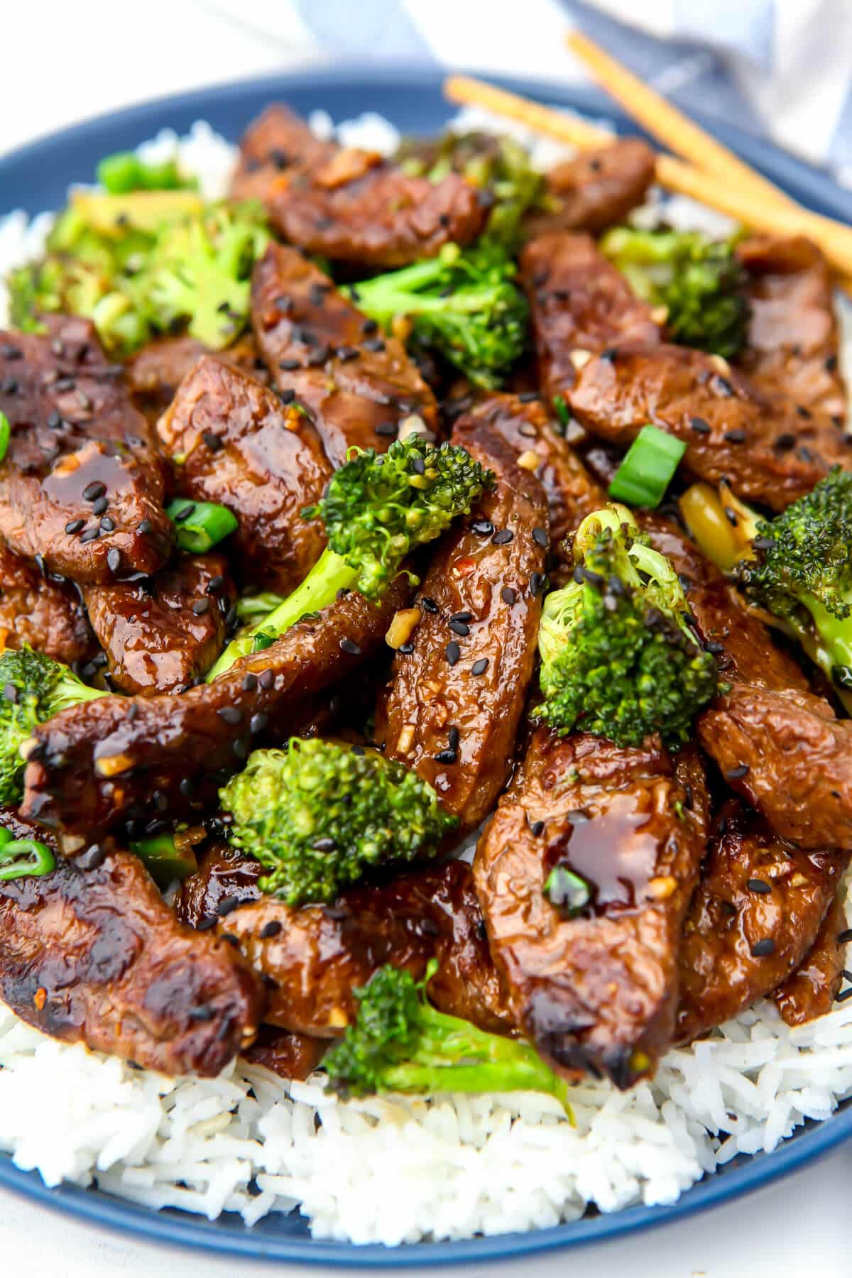 Vegan beef and broccoli served over a bed of white rice on a blue plate.